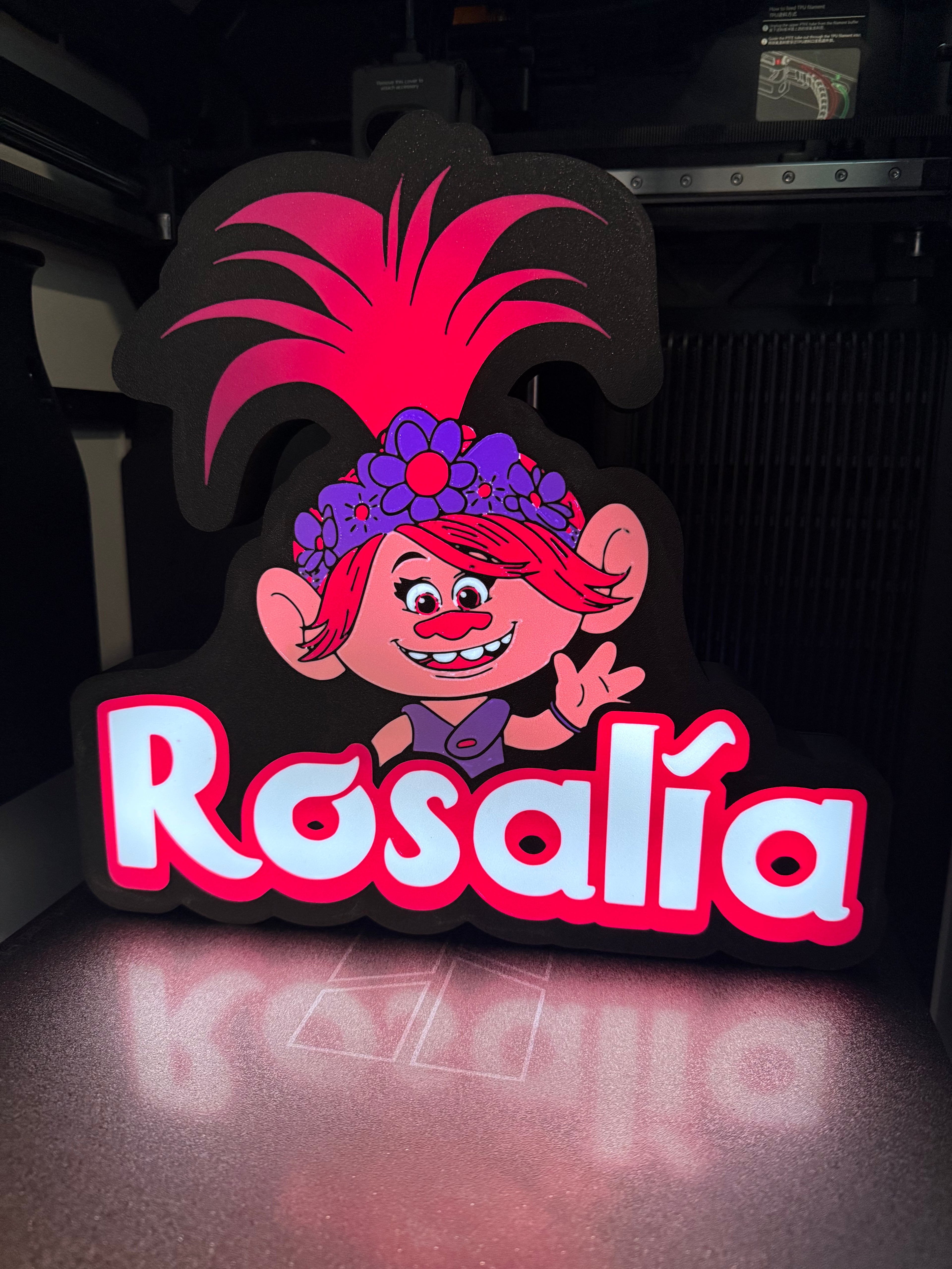 Decorative sign with Trolls cartoon character  Poppy and 'Rosalía' text on a dark background